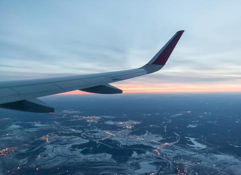 Airplane flight at sunset or dawn. Aircraft's wing and land seen through the illuminator. View from the window of the plane. Airplane, Aircraft. Traveling by air.