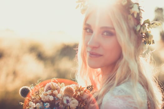 Beautiful young woman portrait in a white dress in boho style with a floral wreath in the summer in the field. Selective soft focus.