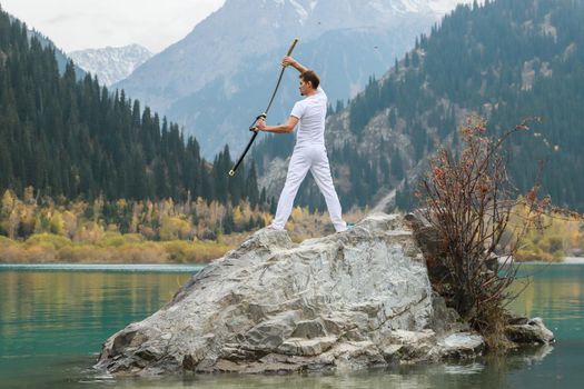 A young man stands on a large stone and holds a Japanese sword in his hands