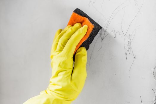 Female hand wearing the protective ruber gloves erasing the child drawings from the dirty wall
