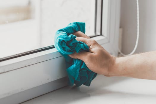 Man cleaning the windowsill with a blue cloth. Doing chores at home