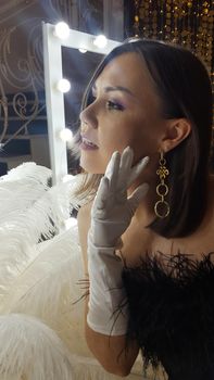 Beautiful asian young woman and decorative ostrich feathers on a gold table next to a make-up mirror. Get ready for the getsby party