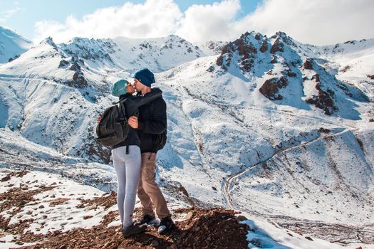A kiss between a man and a woman amid snow mountains. Holiday in mountains.