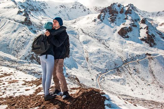 A young man hugs his wife on a background of snowy mountains. Holidays in the mountains.