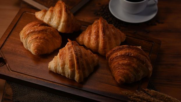 Delicious fresh croissants and coffee cup on wooden board.