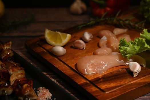 Raw tender chicken on cutting board with spices, herbs and vegetables for grill and bbq. Selective focus.