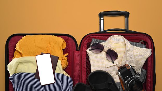 Open suitcase, smart phone, sunglasses, camera and passport on yellow background for summer holidays. Top view.