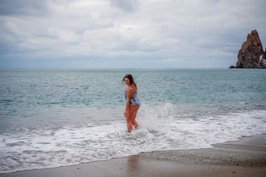 A plump woman in a bathing suit enters the water during the surf. Alone on the beach, Gray sky in the clouds, swimming in winter