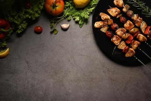 Plate with grilled chicken meat skewers and fresh vegetables on dark stone background. Copy space for your text.
