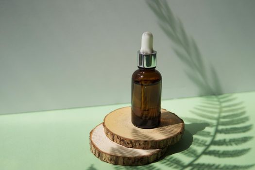 Cosmetic bottle with facial serum on a wooden podium. The concept of zero waste and ecology. A hard shadow from a fern leaf.