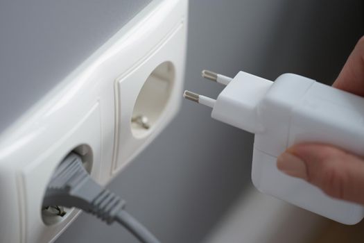 A female hand plugs the power supply unit for a laptop into an outlet, close-up. Uninterruptible power supply, phone charger