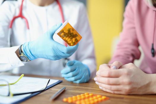 Close-up of therapist hand holding bottle with capsules. Female patient at doctor appointment. Blisters of pills on table. Medical prescription, treatment and healthcare concept