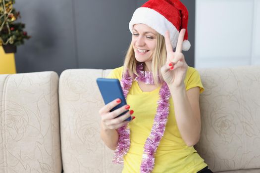 Portrait of smiling blonde woman show peace sign on smartphone, talk to friend or family on video call, congratulate with new year holiday. Christmas, technology, connection concept