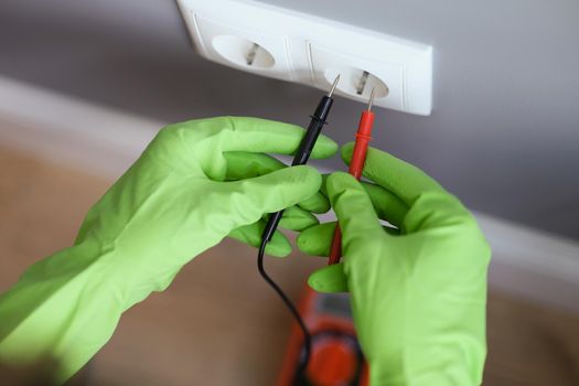 Measuring voltage with a multimeter, hands in rubber gloves close-up. Measuring instrument for electrical repair and maintenance