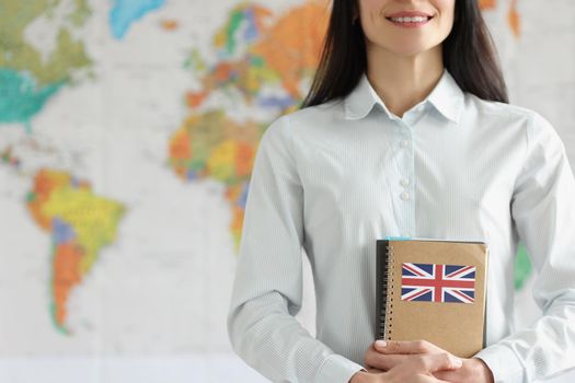 Close-up of young smiling female holding notebooks with britain flag. Cheerful student in shirt. Studying english language concept. World map on background