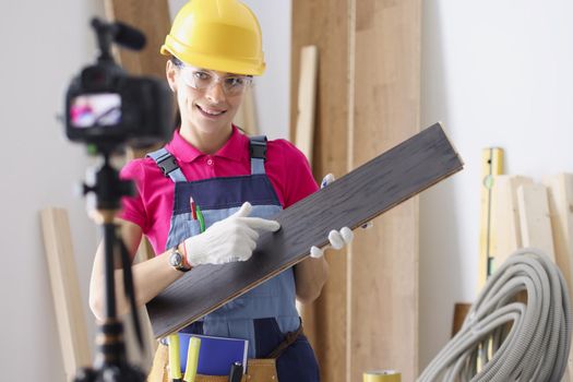 Portrait of professional female worker holding laminate board and showing to camera. Repairer perform construction task, renovation in home. Building blogging and vlogging idea. Redecoration concept