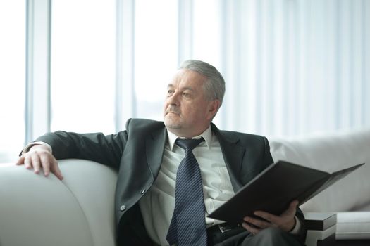 pensive businessman with clipboard sitting on the office couch.