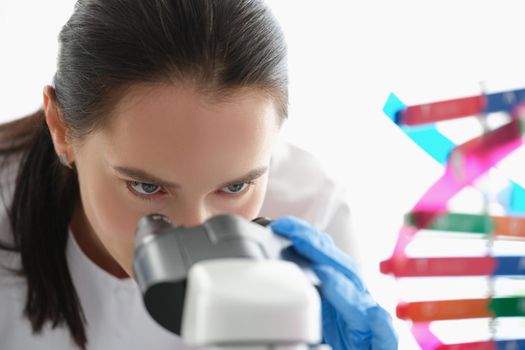 Woman scientist looking through a microscope, studying dna, face close-up. Hereditary information, decoding of the human genome