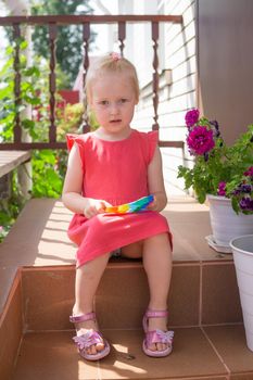 Cute caucasian fair hair girl in pink dress is playing and showing funny trendy silicone antistress colorful toy popit. Kids being kids LGBTQ colors Vertical