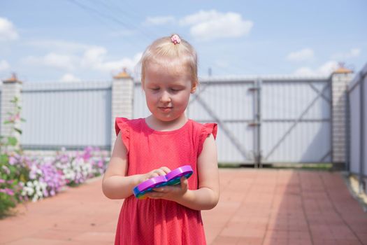 Cute caucasian fair hair girl in pink dress is playing and showing funny trendy silicone antistress colorful toy popit. Push Popper fidget toy is the ideal toy to get rid of your frustration or stress. Kids being kids LGBTQ colors Vertical