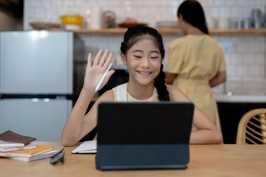 Smiling little asian girl in headphones have video call distant class with teacher using laptop, happy small child wave greeting with tutor, study online on computer, homeschooling concept.