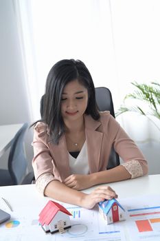 Smiling young businesswoman holding house model. Accounting, property investment concept.