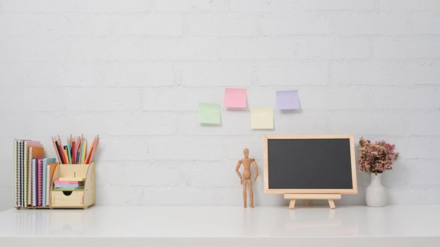 Chalkboard, potted plant and stationery on white table against brick wall. Copy space for your information content.