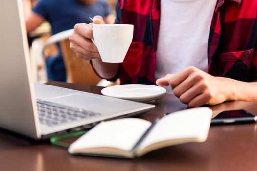 detail of the hands of an unrecognizable man holding a coffee while working from a terrace with his computer, concept of technology and urban lifestyle
