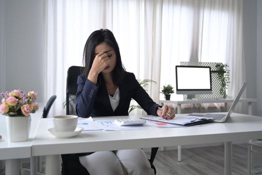 Frustrated female office worker looking worried, tired and overwhelmed while working at office desk.