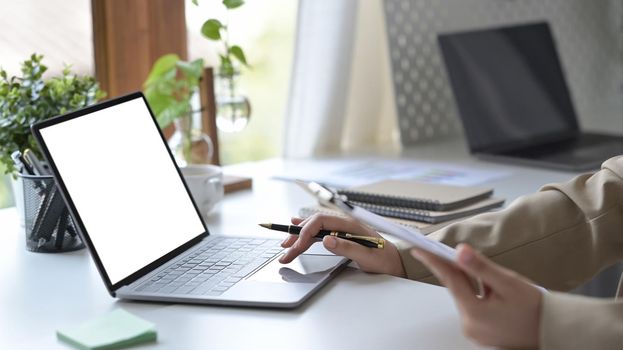 Cropped shot young woman holding clipboard and typing on laptop computer.