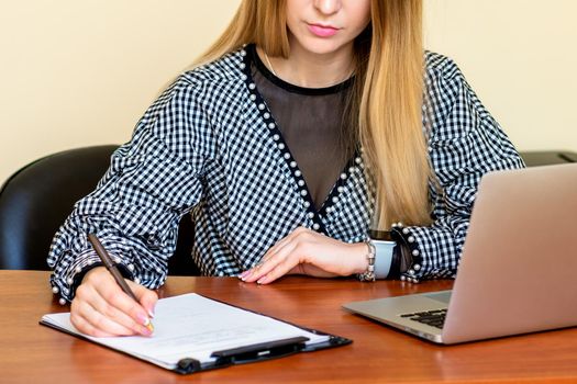 Business woman is writing on a document with laptop at home office.