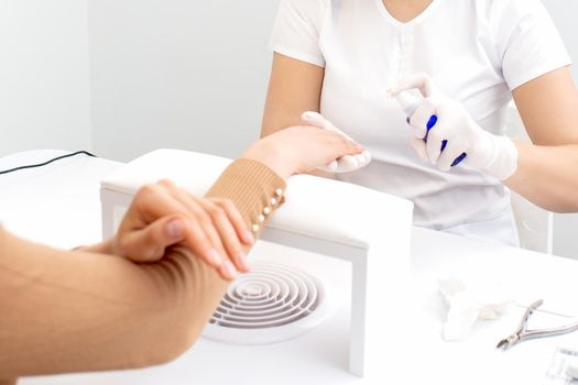 Hands of manicurist disinfecting the fingers of woman client by spray in manicure studio.