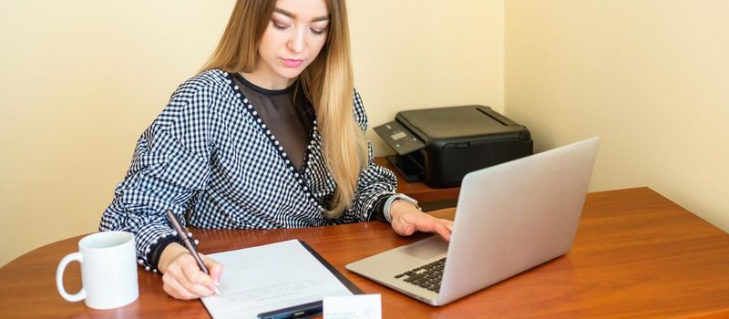 Business woman is writing on a document with laptop at home office.