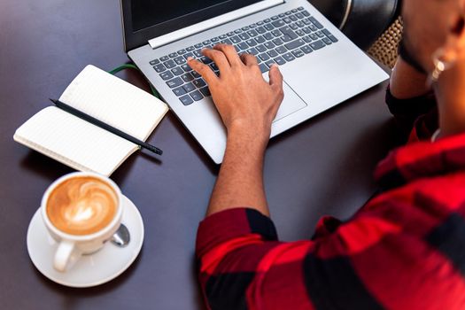 hand of an unrecognizable man typing on a laptop computer at a coffee shop table, concept of technology and urban lifestyle