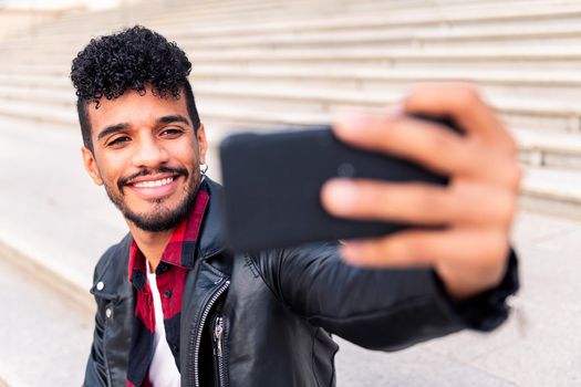 happy young latin man smiles as he takes a selfie with his smart phone, concept of technology and urban lifestyle