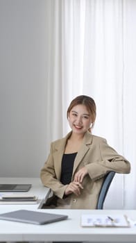 Portrait of confident young entrepreneur sitting at modern workplace and smiling to camera.