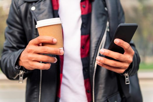 detail of the hands of an unrecognizable young man consulting his phone with a take away coffee, concept of technology and urban lifestyle