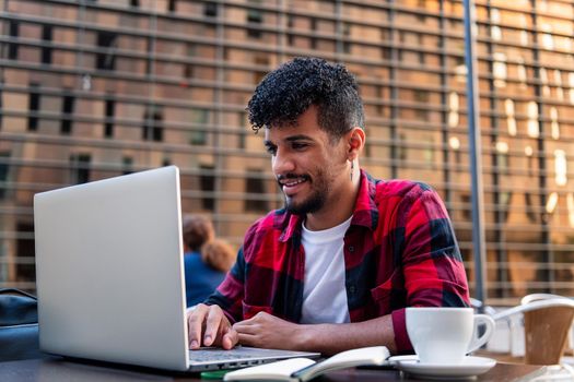 young latin man working with his computer on the terrace of a coffee shop, concept of technology and urban lifestyle