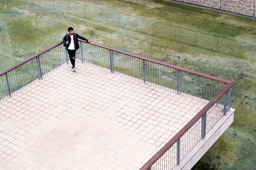young urban man resting leaning on the railing next to the lake in a park of the city, concept of urban lifestyle