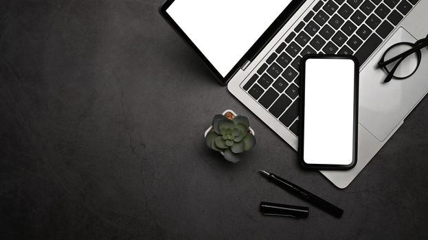 Modern workplace with smart phone, laptop computer and glasses on dark background.