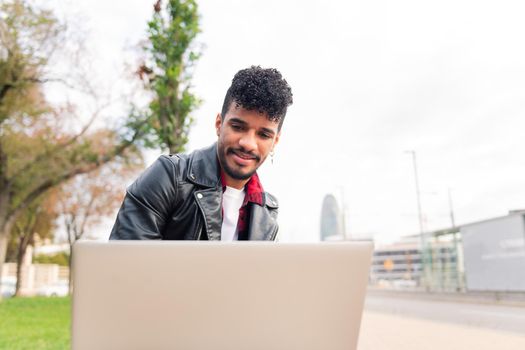 young latin man working on his laptop computer sitting on a city bench, concept of technology and urban lifestyle