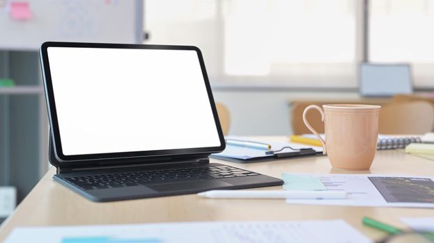 Digital tablet with wireless keyboard, coffee cup and financial documents on office desk.