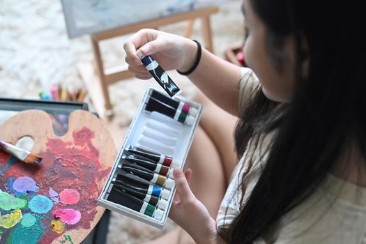 Cropped shot of little girl hand choosing acrylic paint tube for her artwork.
