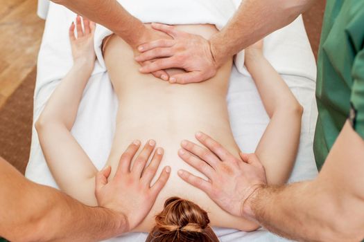 Back massage of woman in four hands by two massage therapists in massage salon.