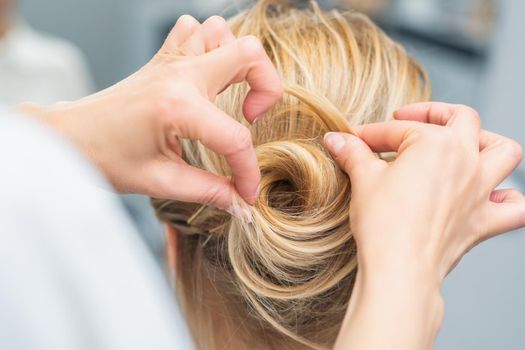 Close up rear view of hairdresser making hairstyle for long hair of blonde woman.