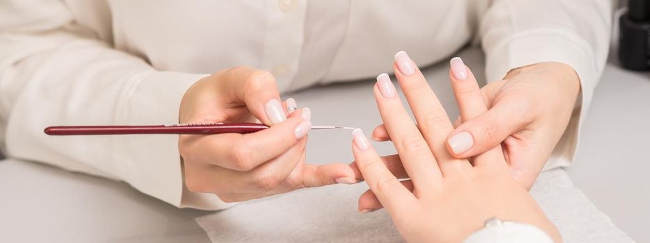 Hand of young woman receiving french manicure by beautician at nail salon.