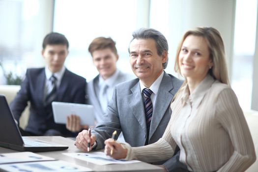 Portrait of mature business man smiling during meeting with colleagues in background.