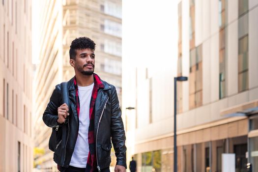 stylish young latin student walking in the city with his backpack, concept of urban lifestyle