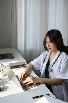 Attractive female doctor is working with documents and laptop in her medical office.