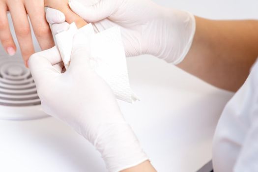 Hands of manicurist wiping nails with a paper napkin in salon, close up.
